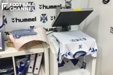 柴崎のネーム入りユニフォーム製作作業真っ最中。左隣には背番号のシートが山のように積まれていた